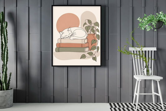 Cat asleep on a stack of books, line art print framed in a room with plants