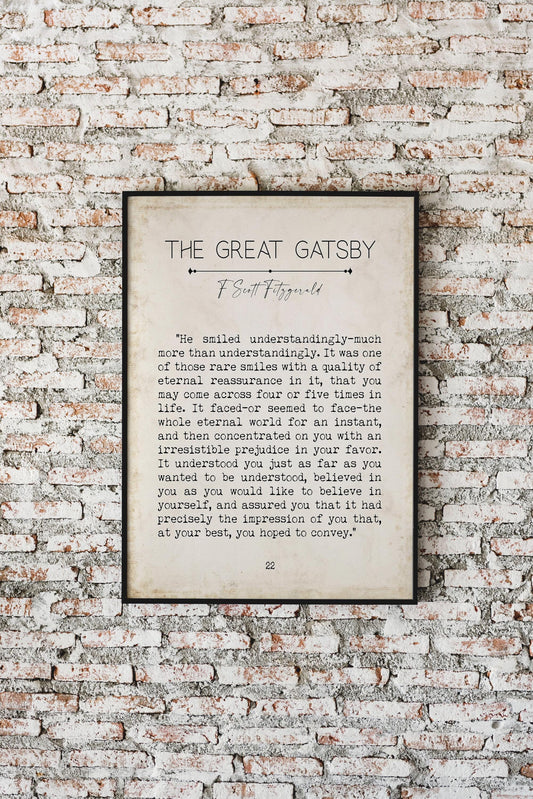 A framed print of a "The Great Gatsby" quote on a brick wall, with text reading: "He smiled understandingly-much more than understandingly. It was one of those rare smiles with a quality of eternal reassurance in it, that you may come across four or
