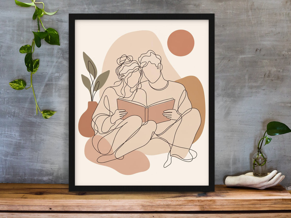 Line art of a couple sitting together reading one book, in blush and terracotta boho colours framed on a desk