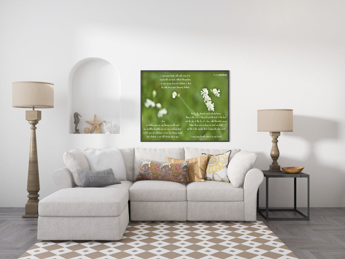 E E Cummings i carry your heart full poem over a photograph of small white wild flowers on green, shown framed in a living room