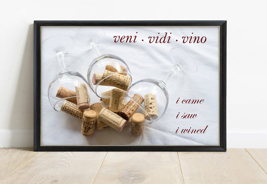 Veni vidi vino, i came i saw i wined, over a photograph of wine glasses and corks, in a black frame