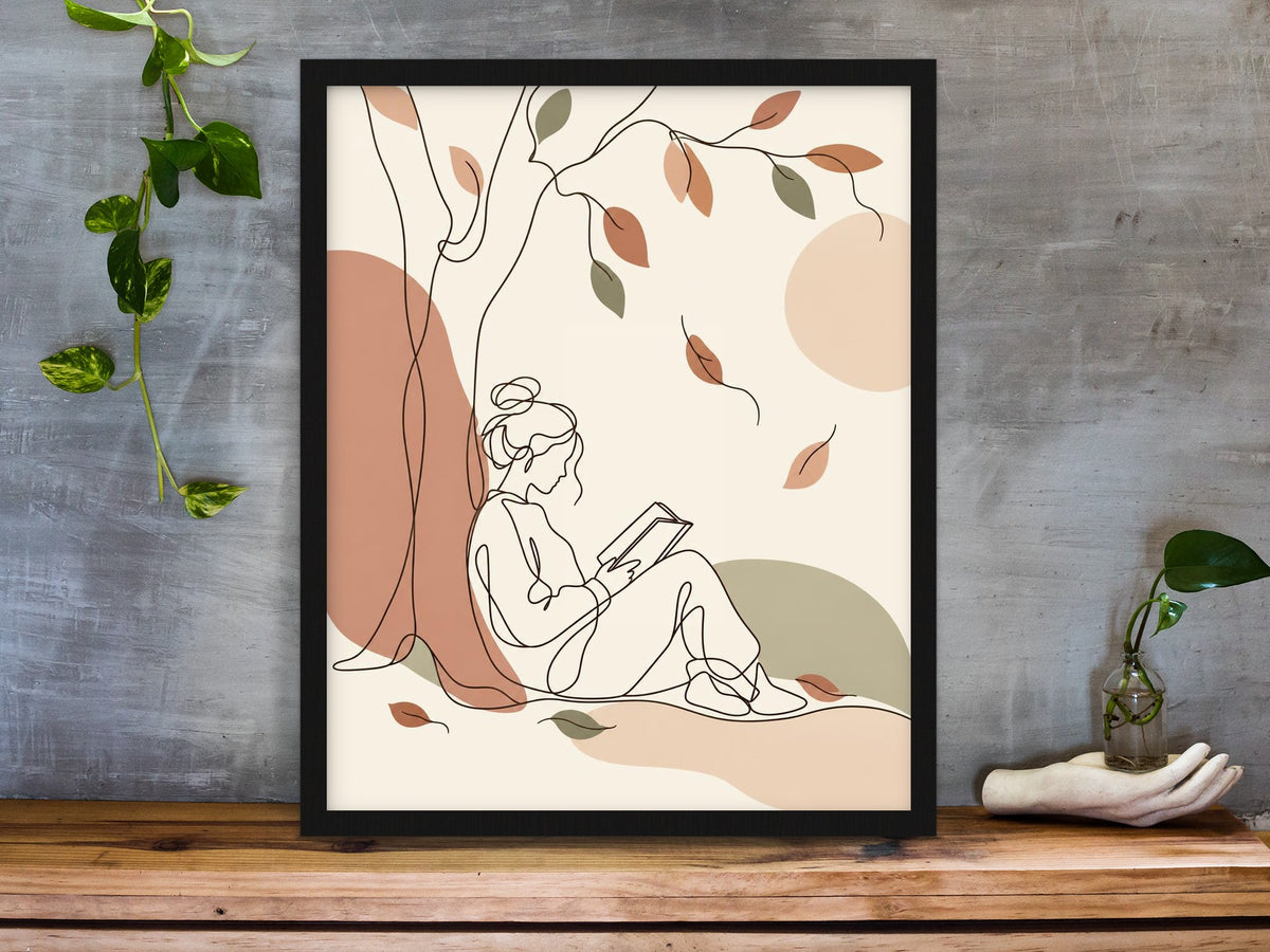 Line art of a woman reading under a tree with falling autumn leaves in boho colours framed on a desk