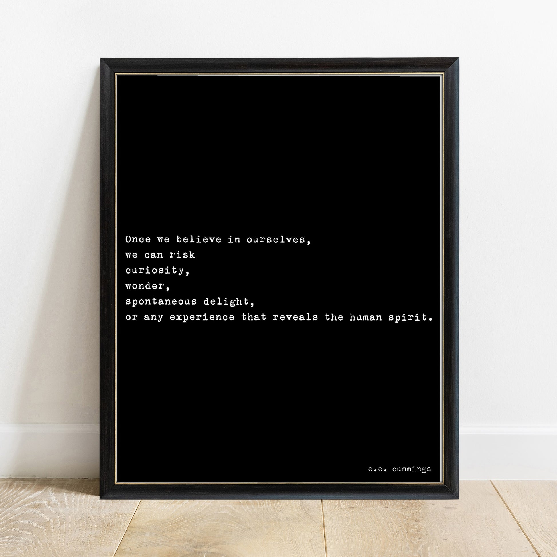 E.E. Cummings once we believe in ourselves quote print in a black frame, black background