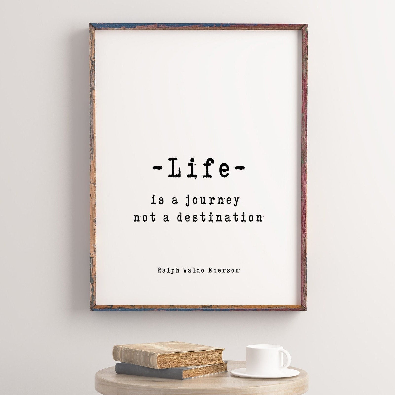 May include: A framed print with a white background and black text that reads 'Life is a journey not a destination' with the author 'Ralph Waldo Emerson' below the quote. The frame is a rustic wood color with a light blue and red paint detail.
