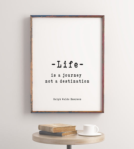 May include: A framed print with a white background and black text that reads 'Life is a journey not a destination' with the author 'Ralph Waldo Emerson' below the quote. The frame is a rustic wood color with a light blue and red paint detail.