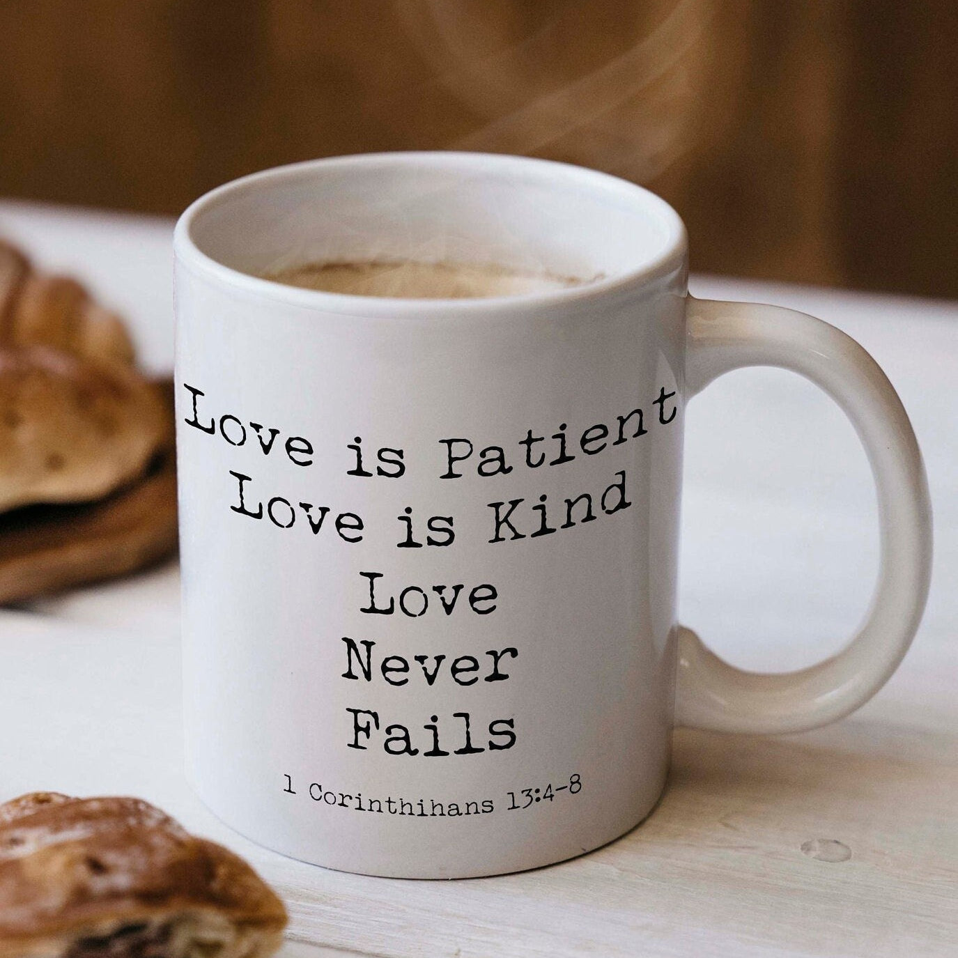 May include: A white ceramic coffee mug with black text that reads 'Love is Patient Love is Kind Love Never Fails 1 Corinthians 13:4-8'.