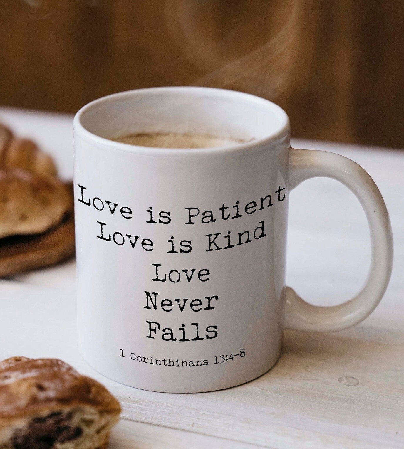 May include: A white ceramic coffee mug with black text that reads 'Love is Patient Love is Kind Love Never Fails 1 Corinthians 13:4-8'.