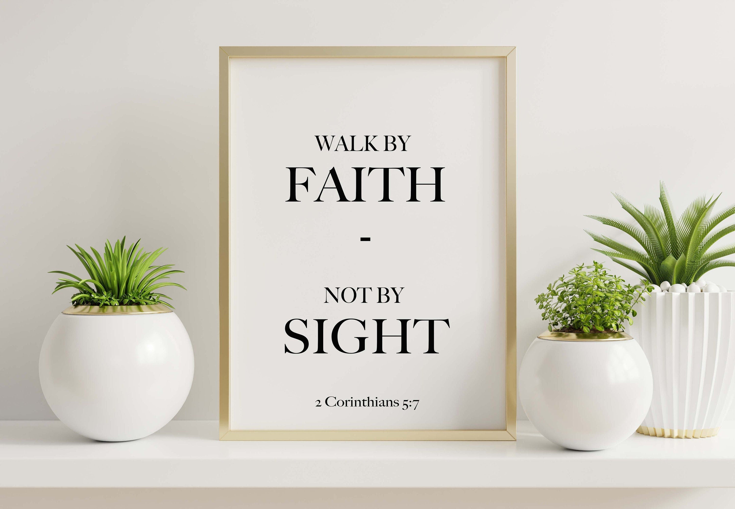 May include: A gold framed print with the text 'Walk by Faith - Not by Sight 2 Corinthians 5:7' on a white background. The print is on a white shelf with two white round planters with green plants.