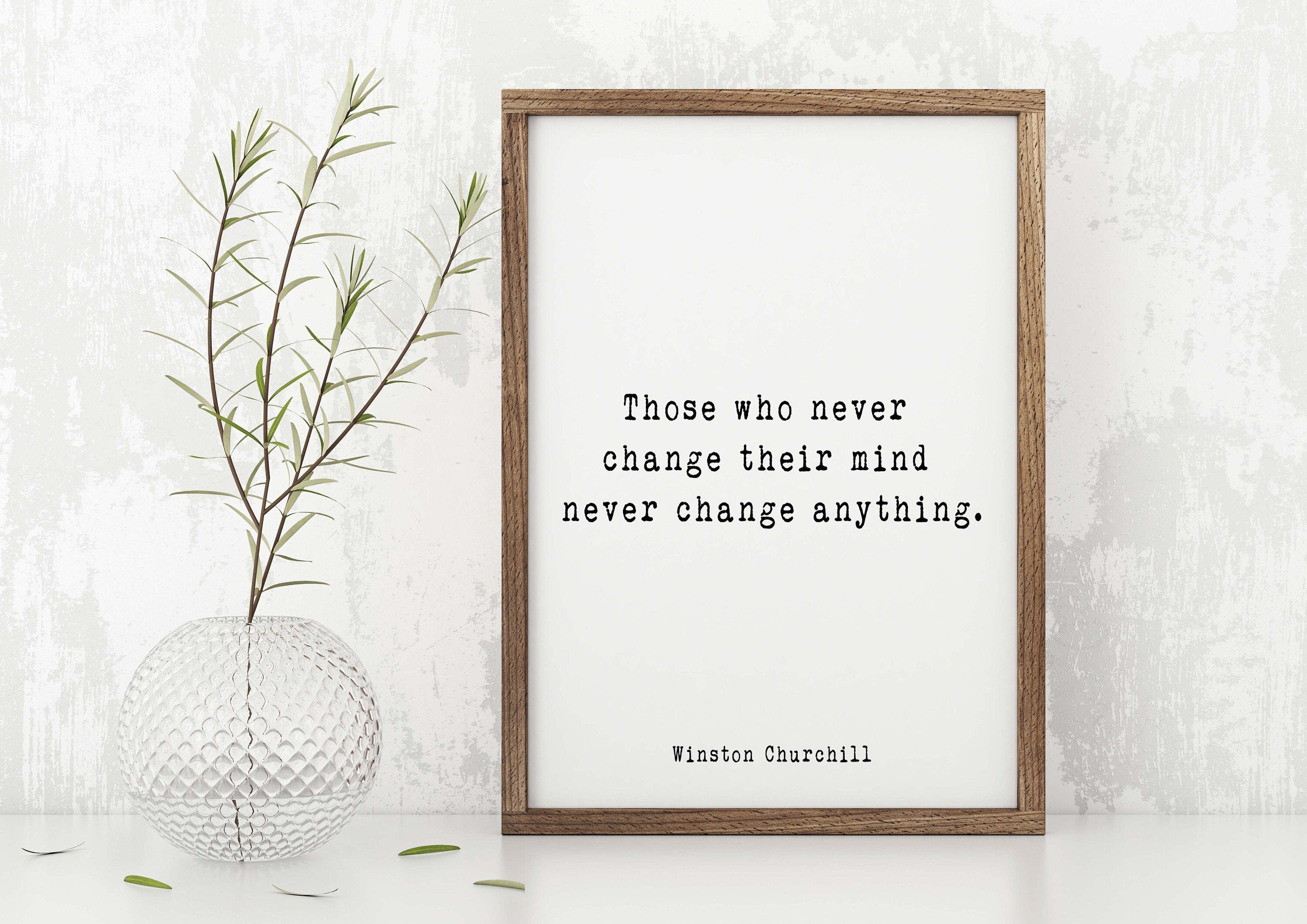 May include: A framed print with a white background and black text that reads 'Those who never change their mind never change anything.' The text is attributed to Winston Churchill. The frame is brown wood and the print is sitting on a white surface.