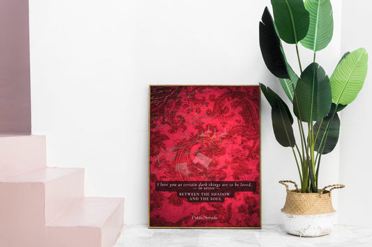 May include: A framed art print with a red abstract design. The print features a quote in a black font: 'I love you as certain dark things are to be loved, in secret, BETWEEN THE SHADOW AND THE SOUL.' The print is displayed next to a large green plant in a woven basket.