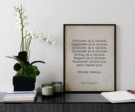 May include: A black framed print with a beige background and white text that reads: 'Attitude is a choice. Happiness is a choice. Optimism is a choice. Kindness is a choice. Giving is a choice. Respect is a choice. Whatever choice you make makes you. Choose wisely. Roy T. Bennett' The print is sitting on a black surface with a white orchid plant in a black planter and two glass candle holders with green candles.
