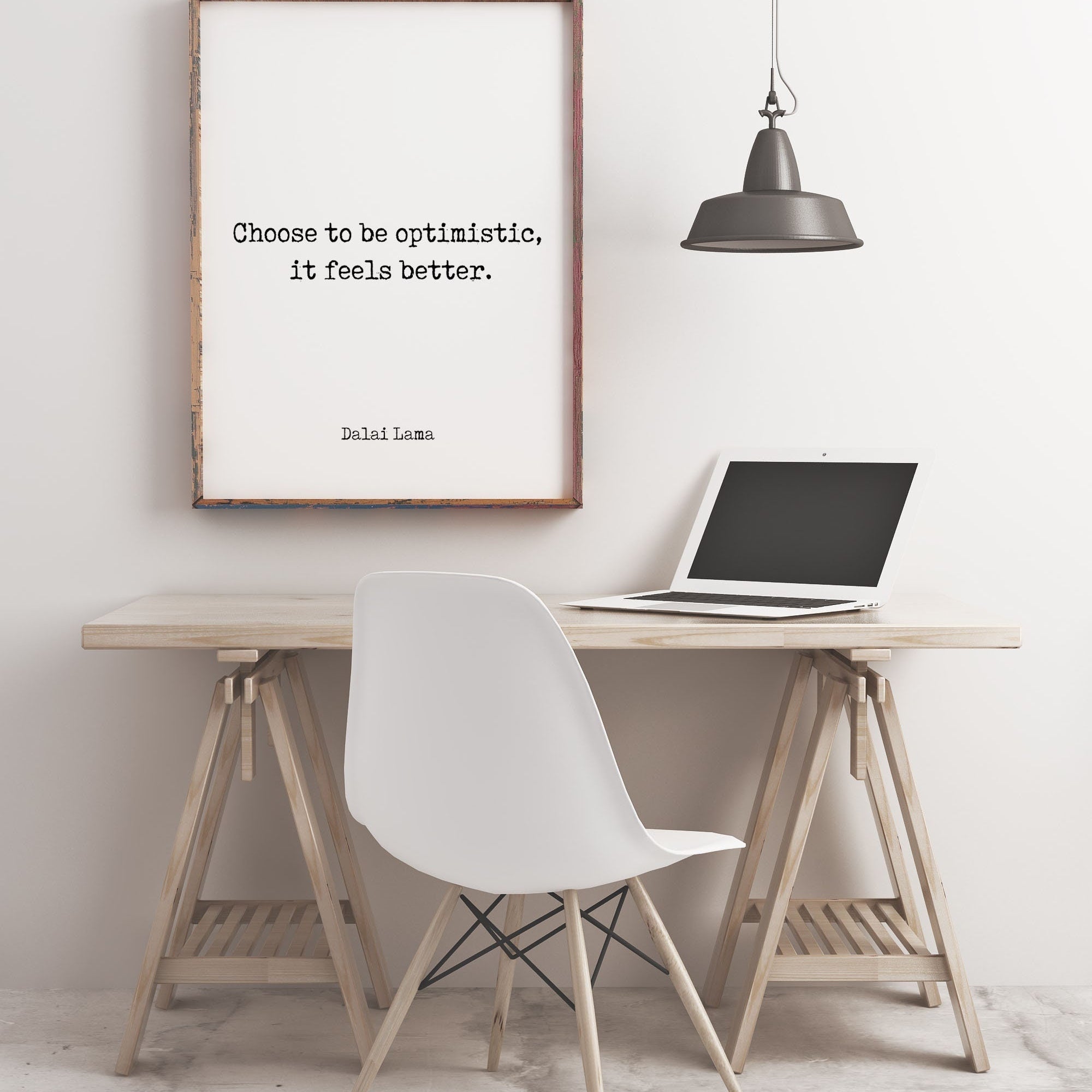 May include: A framed quote on a white wall that reads 'Choose to be optimistic, it feels better. Dalai Lama.'  A laptop is on a wooden desk with a white chair. A black pendant light hangs above the desk.