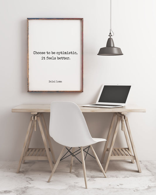 May include: A framed quote on a white wall that reads 'Choose to be optimistic, it feels better. Dalai Lama.'  A laptop is on a wooden desk with a white chair. A black pendant light hangs above the desk.