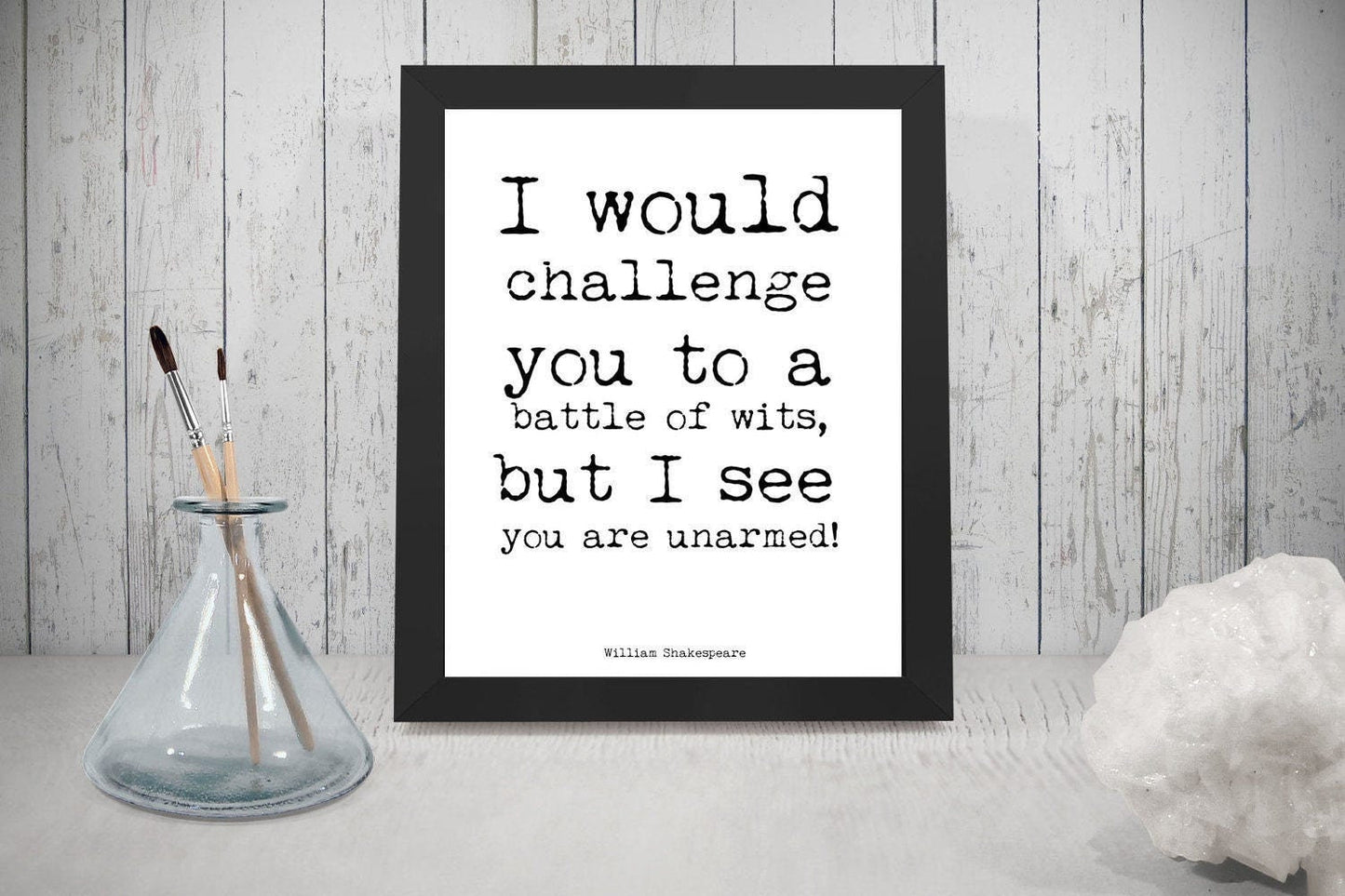 May include: A black framed print with a white background and black text that reads 'I would challenge you to a battle of wits, but I see you are unarmed!' The text is in a typewriter font. The text is attributed to 'William Shakespeare'.