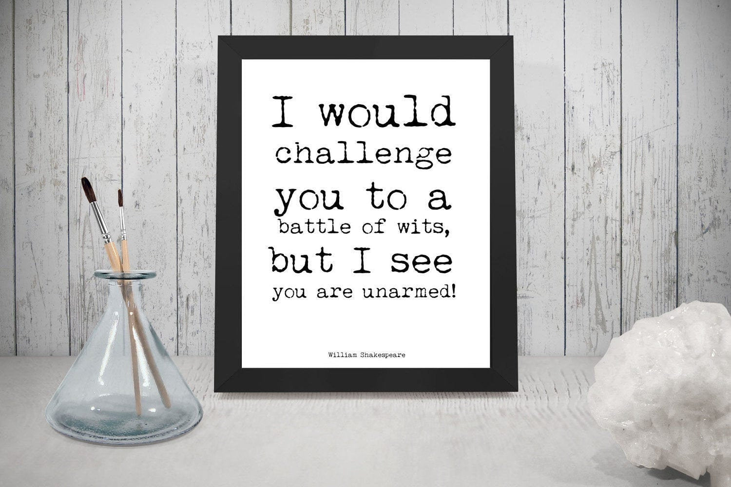 May include: A black framed print with a white background and black text that reads 'I would challenge you to a battle of wits, but I see you are unarmed!' The text is in a typewriter font. The text is attributed to 'William Shakespeare'.