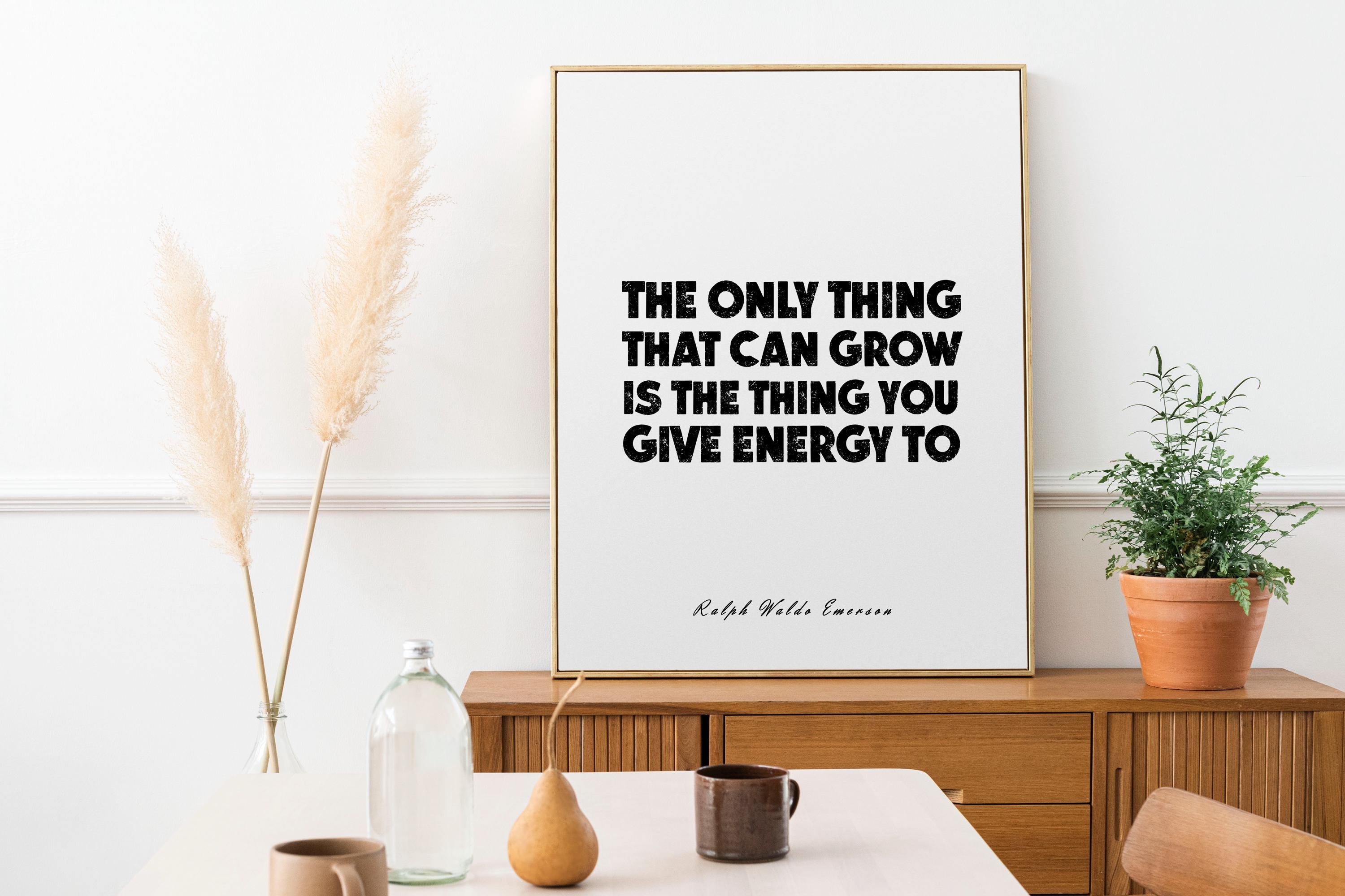 May include: A framed print with the quote "THE ONLY THING THAT CAN GROW IS THE THING YOU GIVE ENERGY TO" in black text. The print is in a gold frame, and is on a wooden cabinet. A small potted plant and decorative items are nearby.