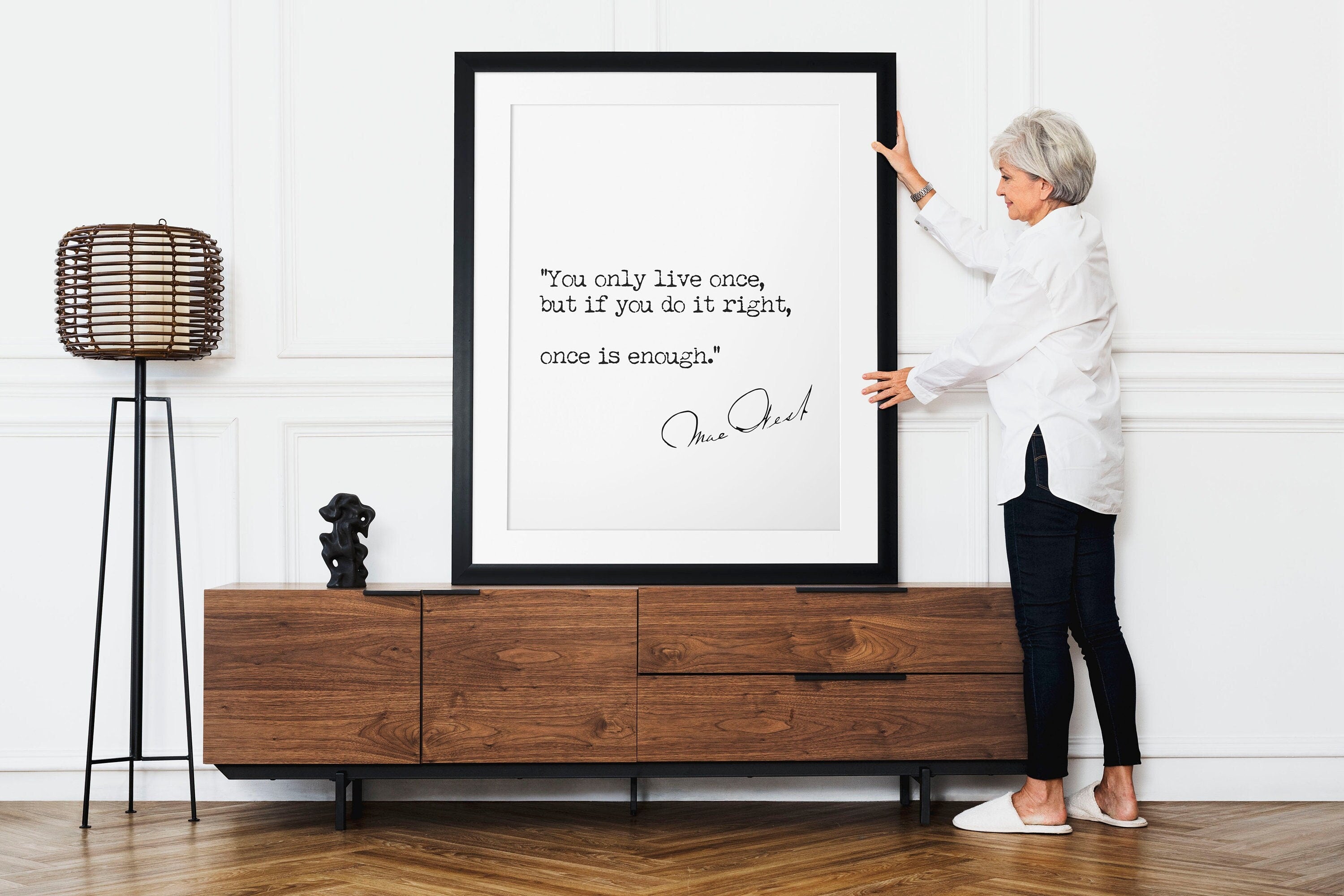May include: A black framed print with a white background and a quote by Mae West: "You only live once, but if you do it right, once is enough."