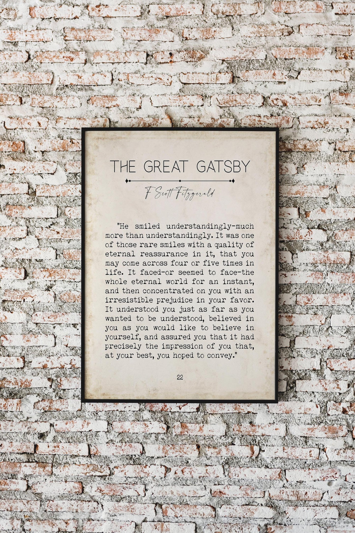 A framed print of a "The Great Gatsby" quote on a brick wall, with text reading: "He smiled understandingly-much more than understandingly. It was one of those rare smiles with a quality of eternal reassurance in it, that you may come across four or