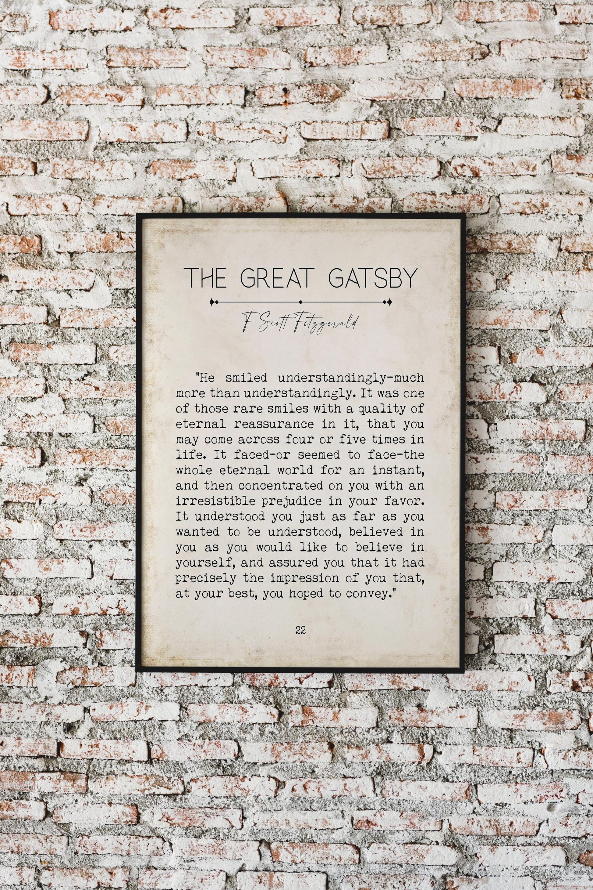 A framed print of a "The Great Gatsby" quote on a brick wall, with text reading: "He smiled understandingly-much more than understandingly. It was one of those rare smiles with a quality of eternal reassurance in it, that you may come across four or
