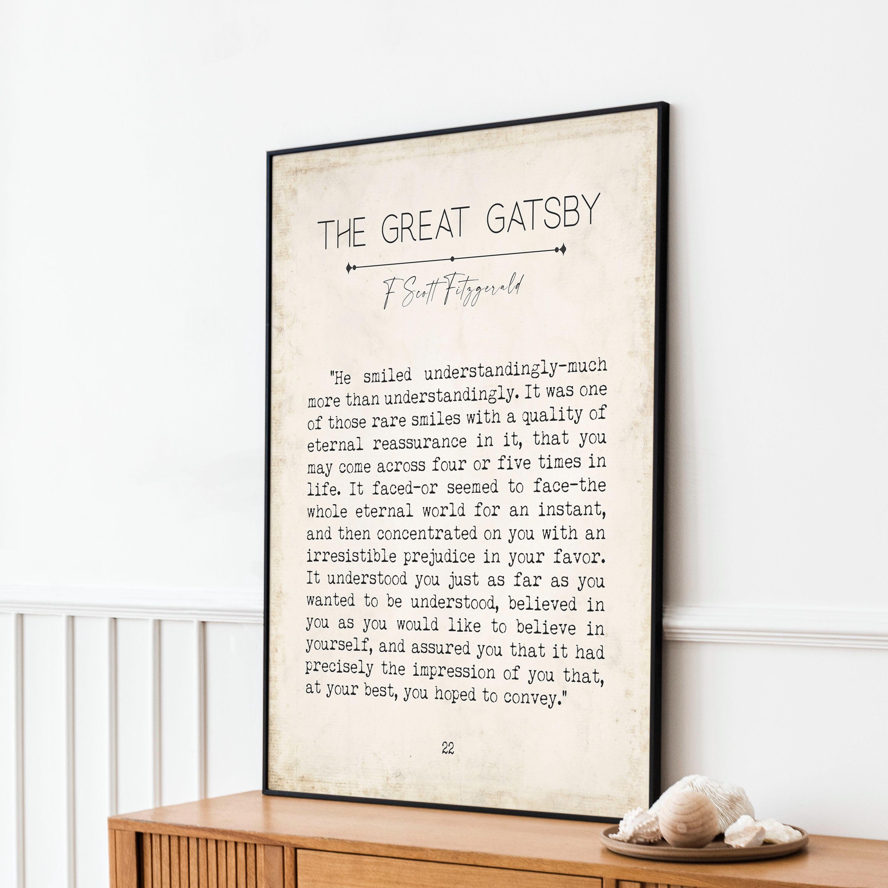 A framed print of a "The Great Gatsby" quote on a wooden dresser, with a decorative shell and a small plant in the foreground.