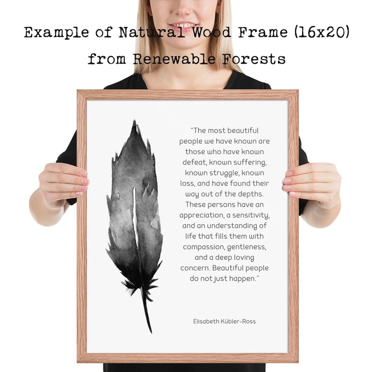 A person holds a light wood-framed print with a black feather illustration and a quote by Elisabeth Kübler-Ross on a white background.