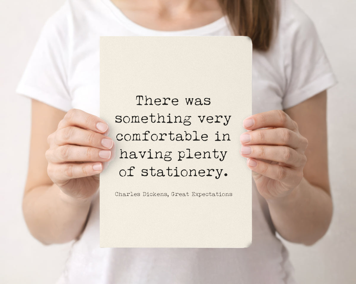 Woman holding a cream softcover journal with the Charles Dickens quote about having plenty of stationery on the front