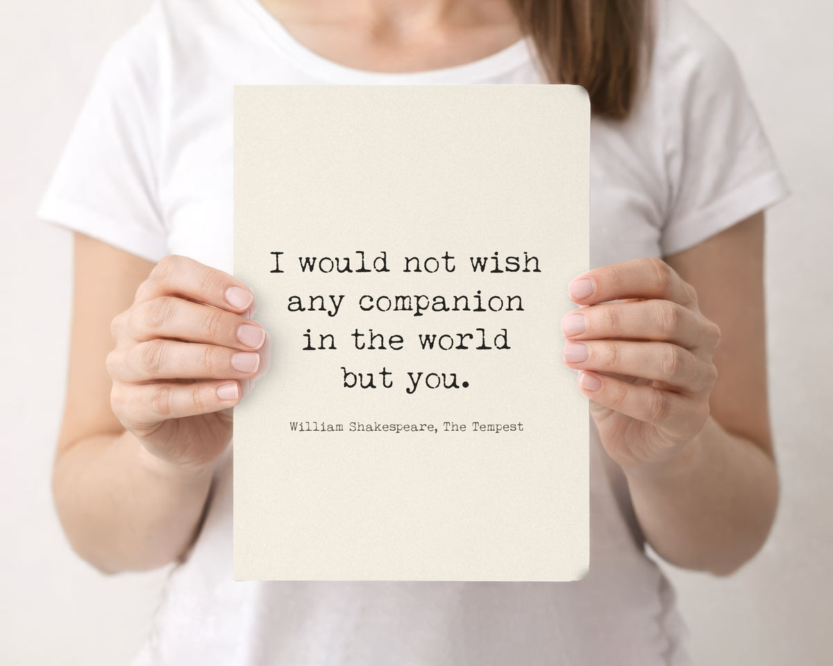 Woman holding a cream softcover journal with the Shakespeare The Tempest I would not wish any companion in the world but you quote on the front