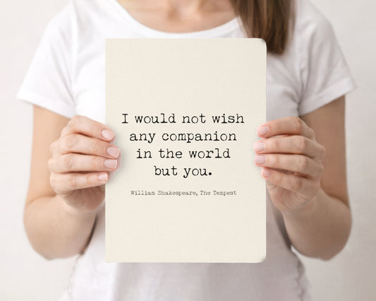 Woman holding a cream softcover journal with the Shakespeare The Tempest I would not wish any companion in the world but you quote on the front