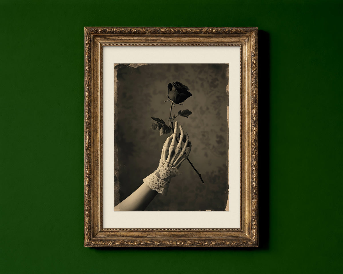 Skeleton hand in a lace cuff holding a black rose, sepia Victorian gothic dark academia print shown in a gold frame for display only; framed prints are sent in a black frame